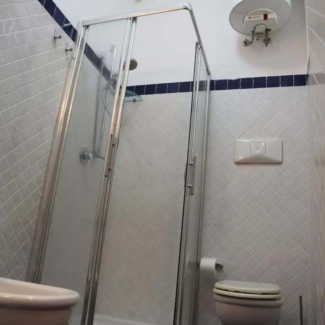 Une salle de bain avec une douche à parois de verre, des toilettes et un luminaire fixé au mur.