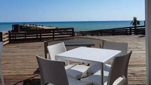 Ein überdachter Außenbereich mit weißen Tischen und Stühlen, mit Blick auf einen Strand und das Meer.