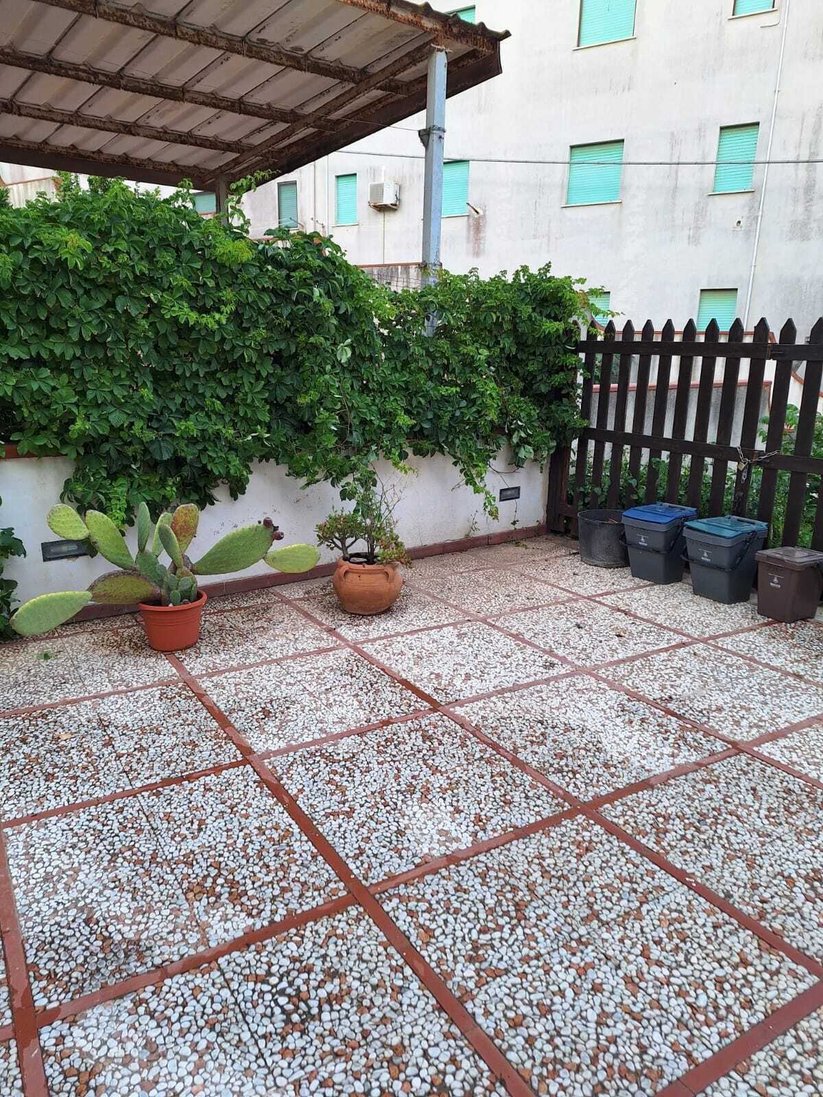 A covered outdoor area with a tiled floor, potted plants, and a black fence.
