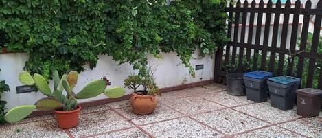 A covered outdoor area with a tiled floor, potted plants, and a black fence.