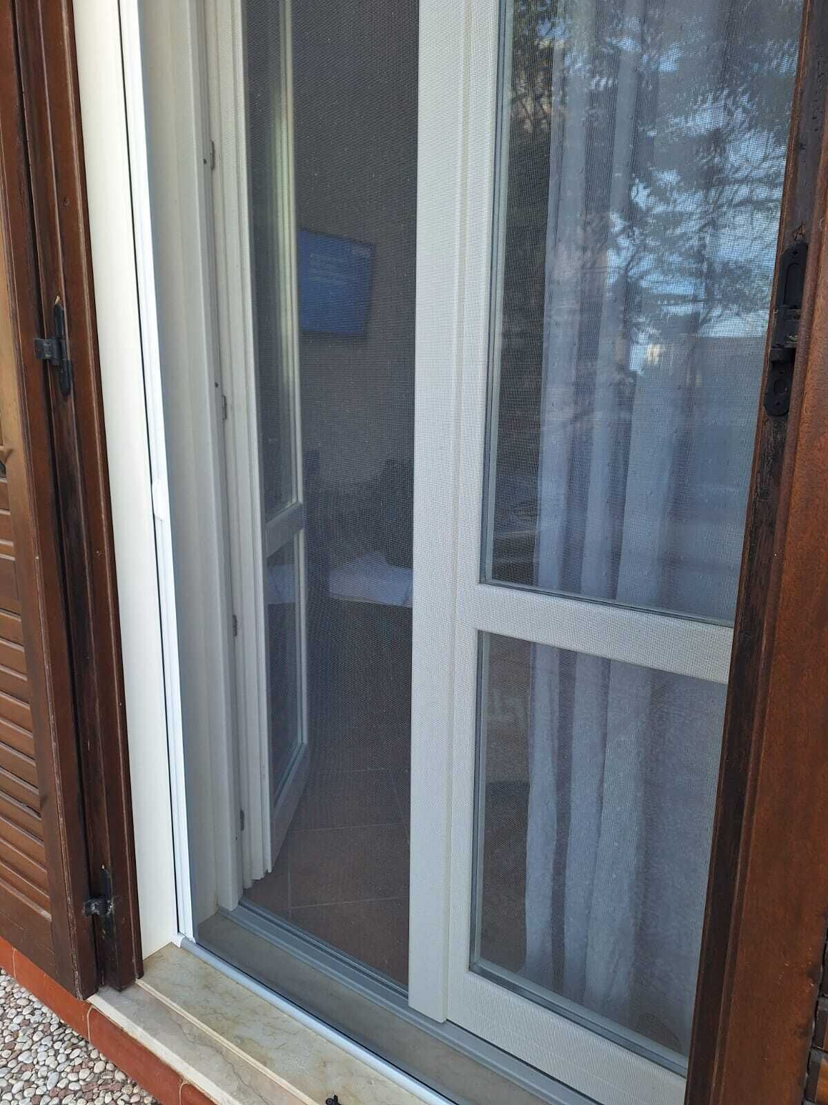 En skjutdörr av glas med ett metallnät, som leder ut till en veranda med ett klinkergolv.