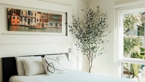 A bedroom with a bed, pillows, a framed painting, and a plant. - Studio 112 - Stay in Style, Stay Central (Ensenada)