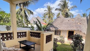 A covered outdoor area with a table and wicker furniture, surrounded by a tiled floor and a decorative railing.