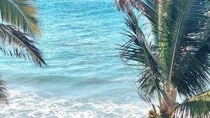 A beach view with palm trees and a sandy area with wooden structures.