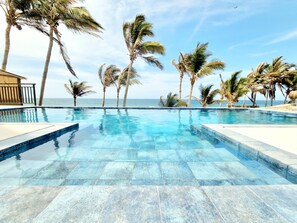 Una piscina cristallina con bordi piastrellati, circondata da palme e vista sull'oceano.