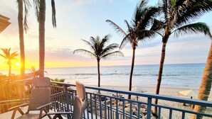 A balcony with metal chairs and a view of the beach and ocean during sunset.