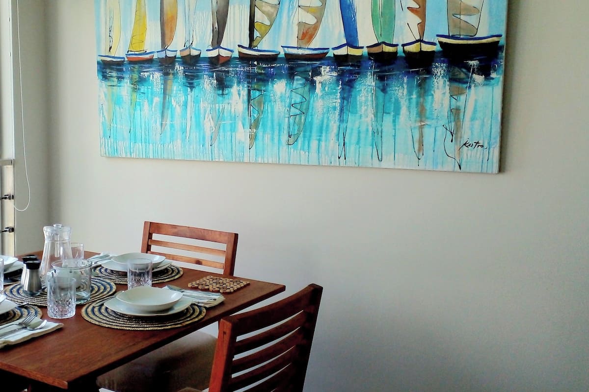 A dining table set with plates, glasses, and cutlery, with a painting of sailboats on the wall.
