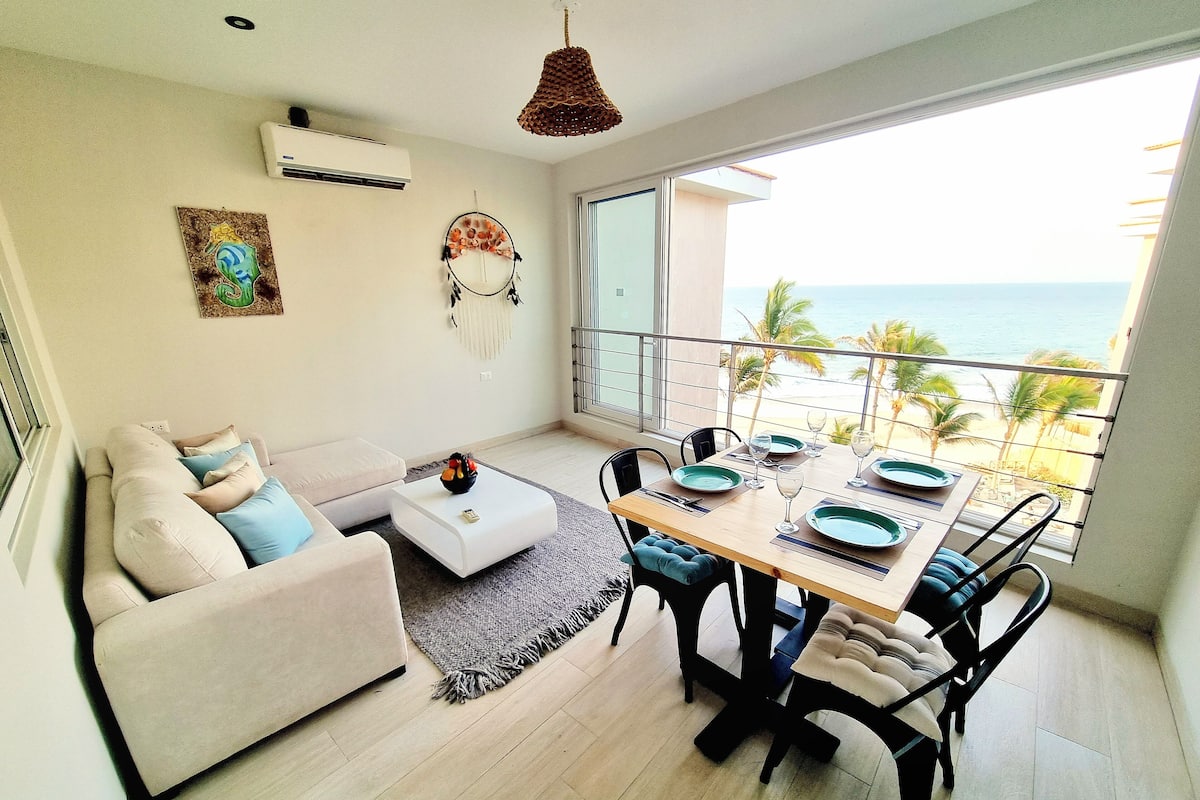 A modern living room with a sofa, a dining table set for four, and a view of the ocean.