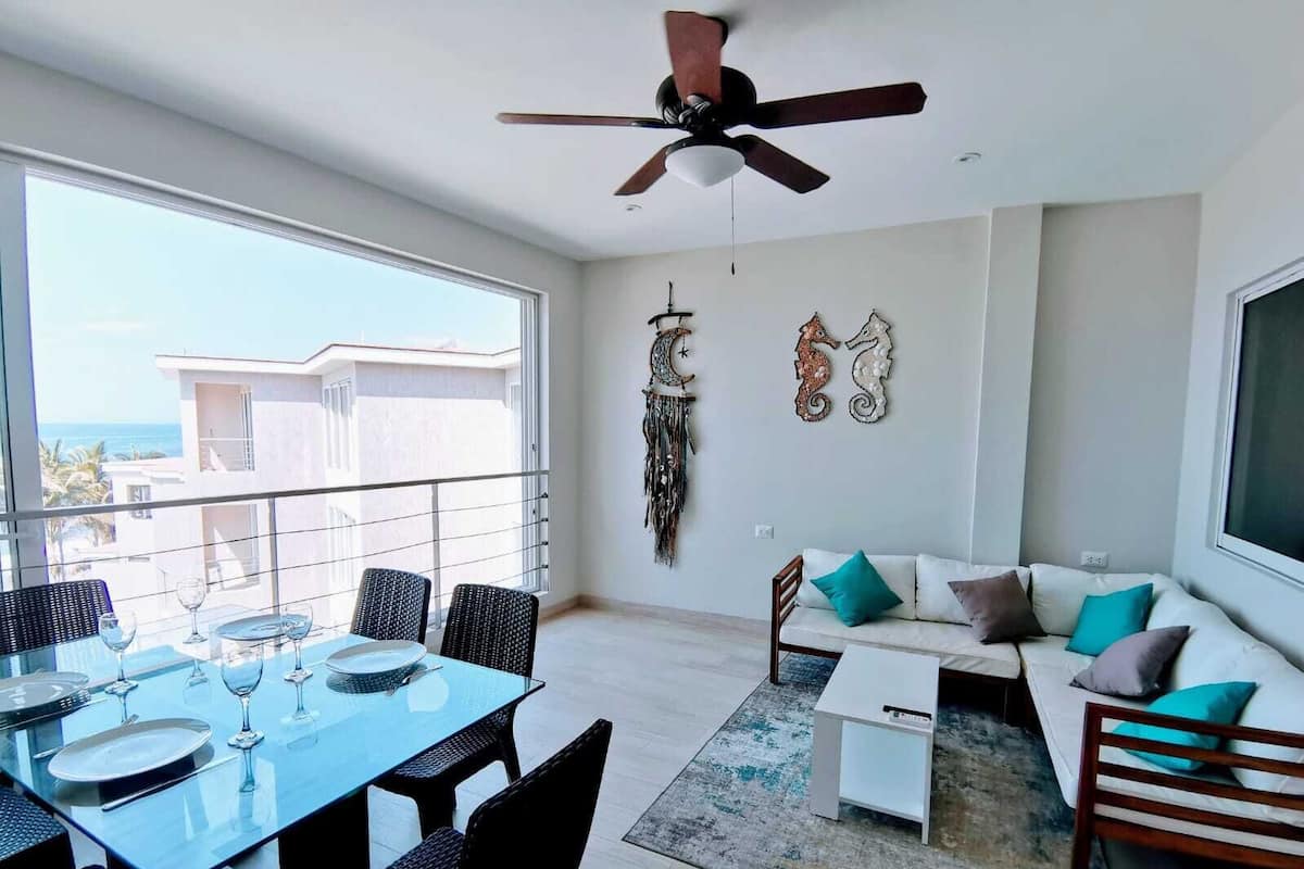 A modern living room with a dining area, a ceiling fan, and a view of the ocean.