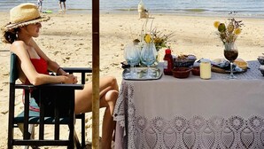 Una mesa en la playa con mantel, una sombrilla y un jarrón con flores.