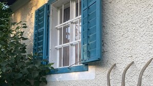 Un bâtiment à l’extérieur texturé, doté d’une fenêtre avec des volets bleus et orné d’un motif en forme de trident.