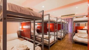 Une chambre de type dortoir avec des lits superposés, un plancher en bois et un mur d’accent rouge.