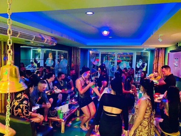 A crowded indoor space with tables and chairs, some people standing and some sitting.