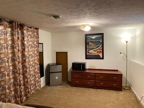 Cozy retreat with a single bed, refrigerator, dresser, and artwork.