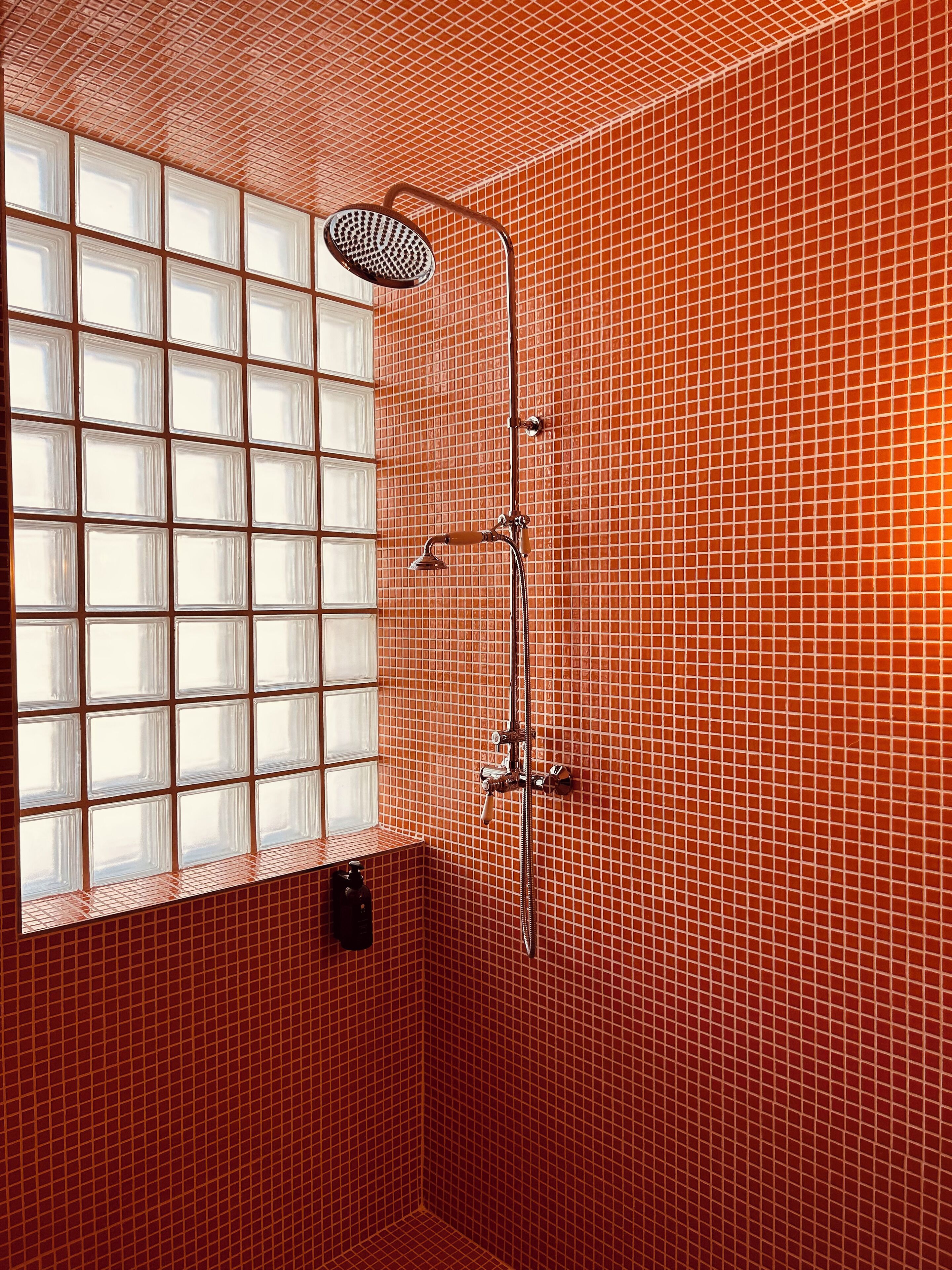 A bathroom with a shower, tiled walls, and a window with frosted glass panels.