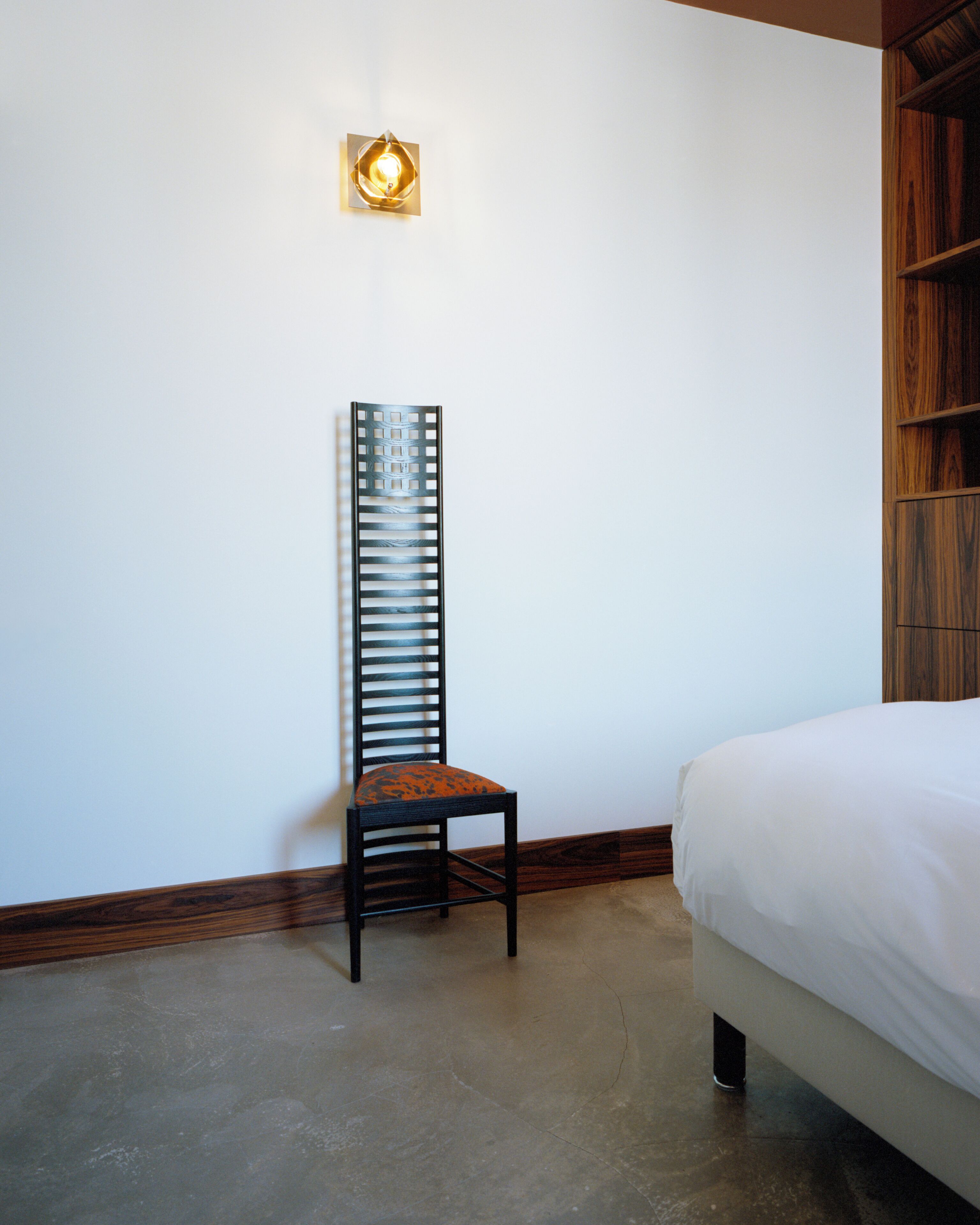 Ein Schlafzimmer mit einem Bett, einem Holzregal und einem Stuhl mit gemustertem Kissen.