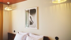 Ett hotellrum med en säng, två sänglampor, ett inramat konstverk på väggen och en sänggavel i trä.