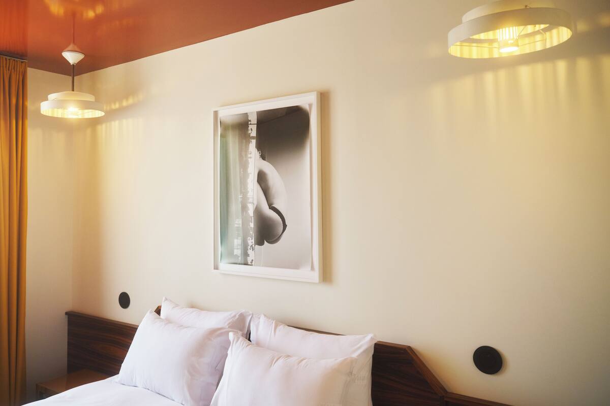 A hotel room with a bed, two bedside lamps, a framed artwork on the wall, and a wooden headboard.