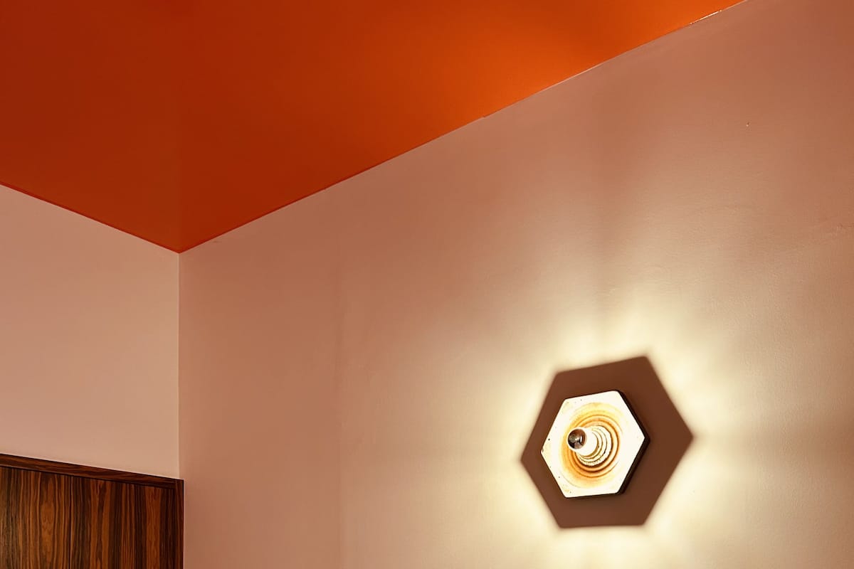 A hotel room with a wooden wardrobe, a bed with white bedding, and a wall-mounted light fixture.
