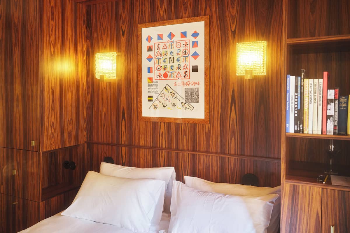 A wooden-paneled room with a bed, two wall-mounted lamps, and a bookshelf.