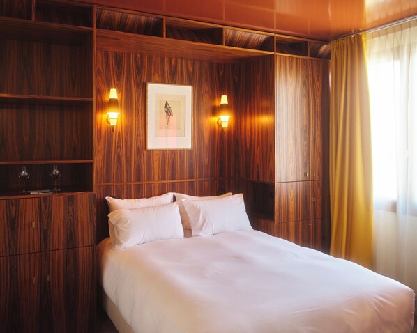 A hotel room with a wooden panel wall, a bed with white linens, two bedside lamps, and a framed picture on the wall. - Hôtel Présent - 200m des Arènes de Arles - Encore Mieux (Arles)