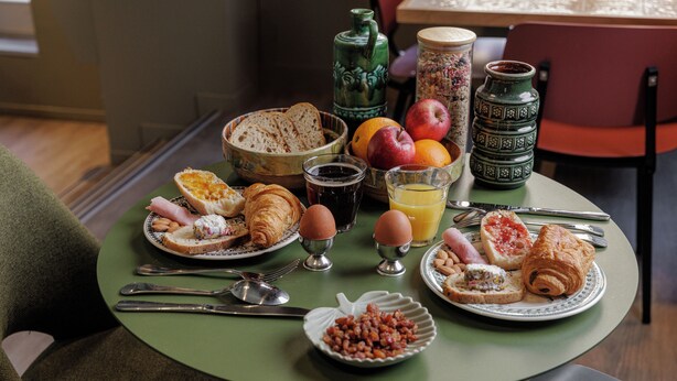 Ett frukostbord med croissanter, ägg, bröd, frukt och drycker.