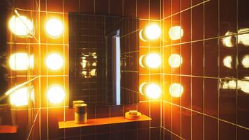 Un baño con un espejo rodeado de varias luces, un lavamanos y un perchero para toallas.