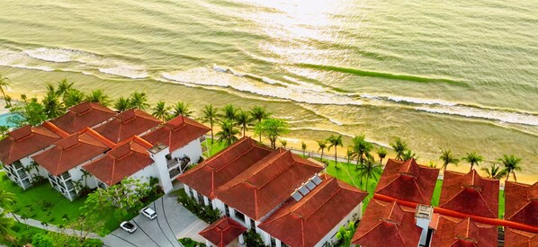 A coastal hotel with red-roofed buildings, a beach, and palm trees. - DANKBAAR RESORT (Quy Nhon Nam)