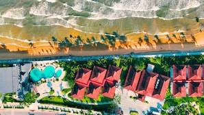 Vista aérea de un resort con playa, piscina y edificios de techos rojos.