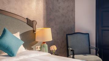 A hotel room with a bed, a chair, a lamp, and a vase with flowers.