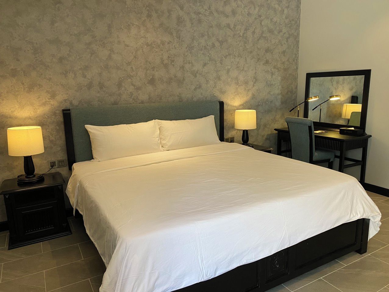 Habitación de hotel con una cama grande, dos lámparas de noche, un escritorio con una silla y un espejo en la pared.