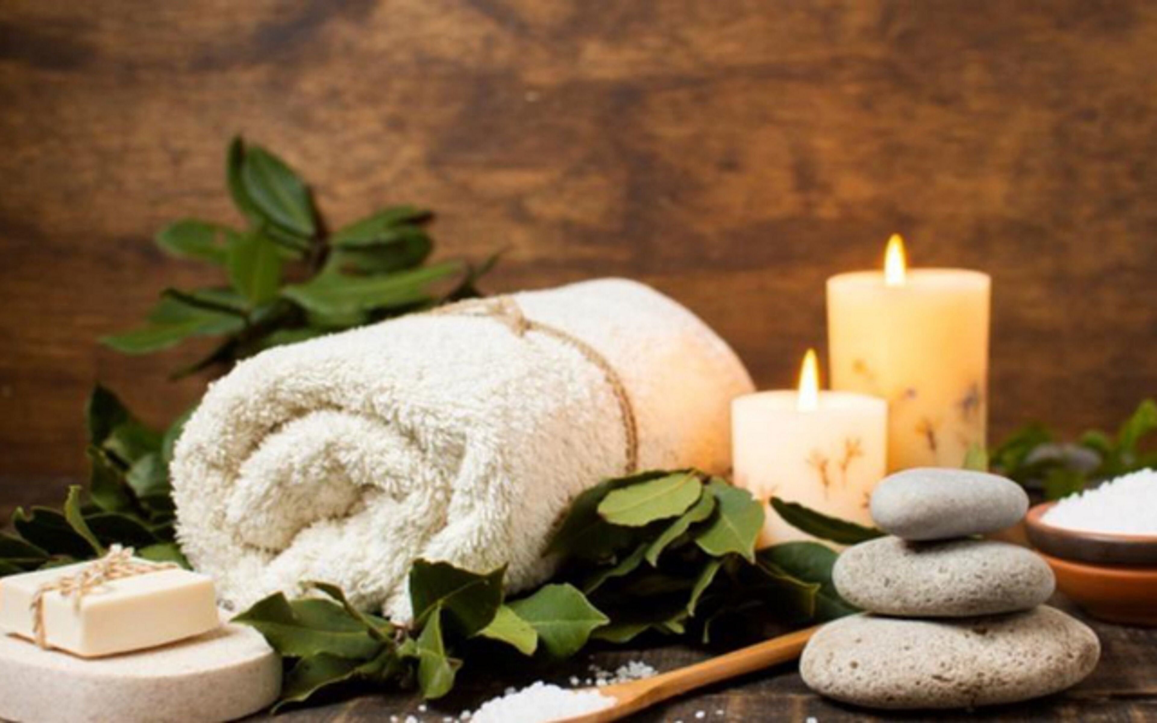 Un ambiente de spa con una toalla enrollada, velas, piedras y una pastilla de jabón.