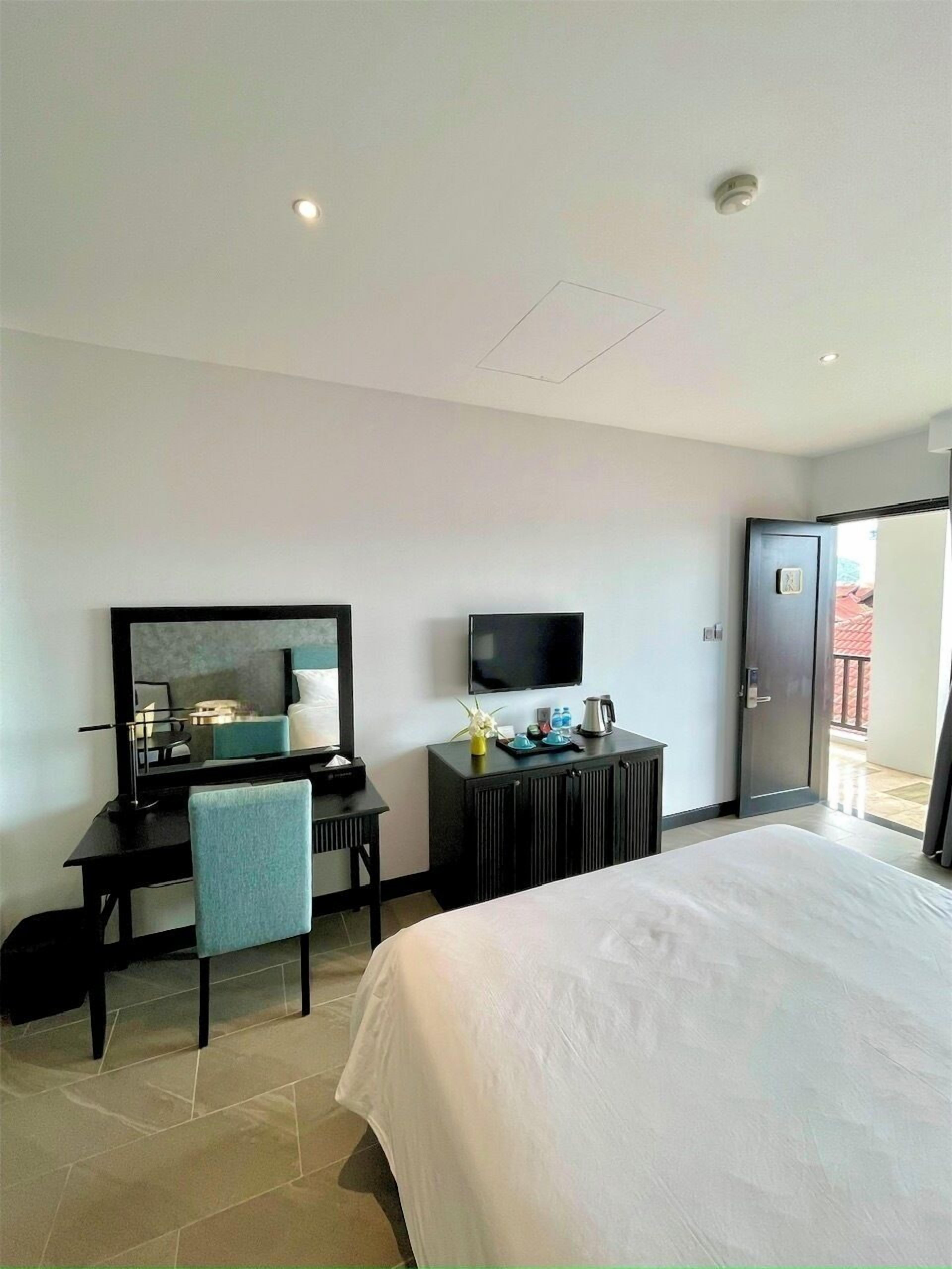 A hotel room with a bed, a desk with a chair, a television, and a door leading to a balcony.