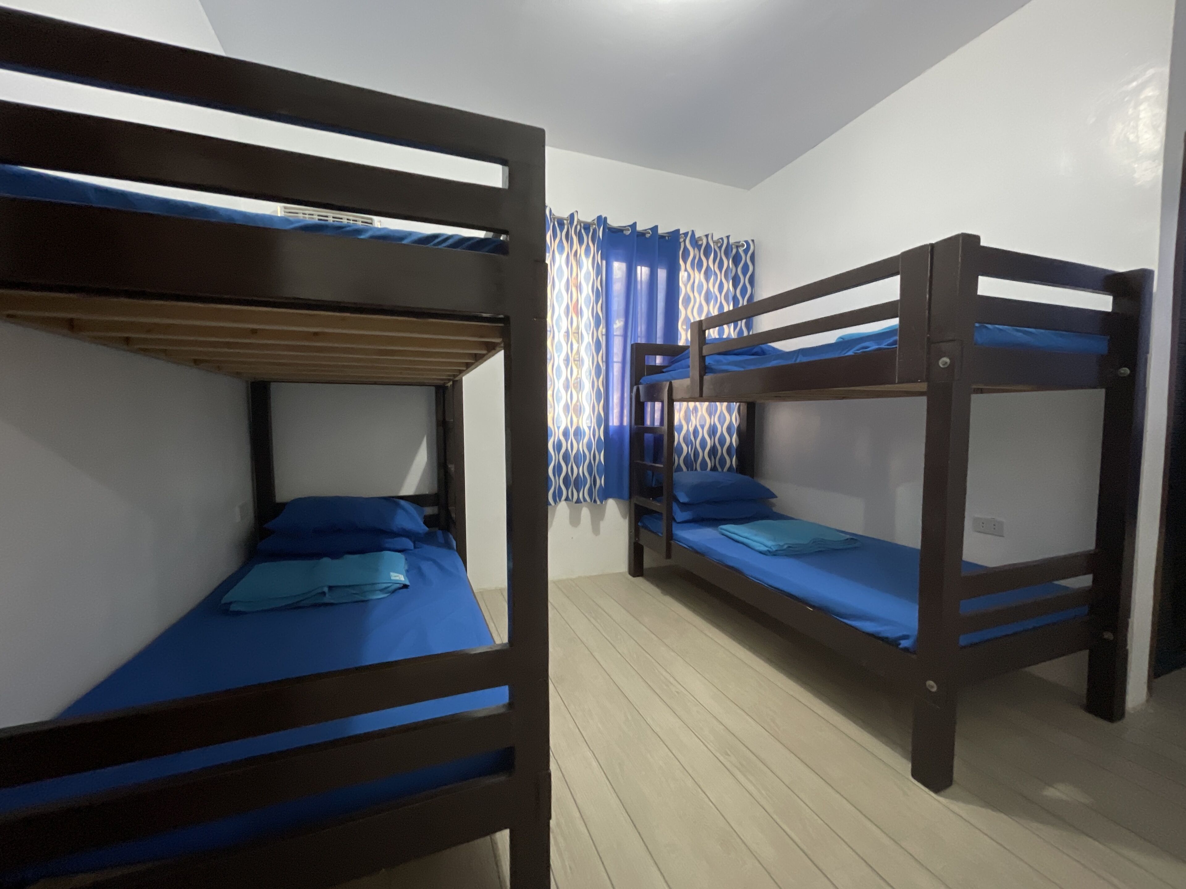 A room with two bunk beds, wooden flooring, and patterned curtains.