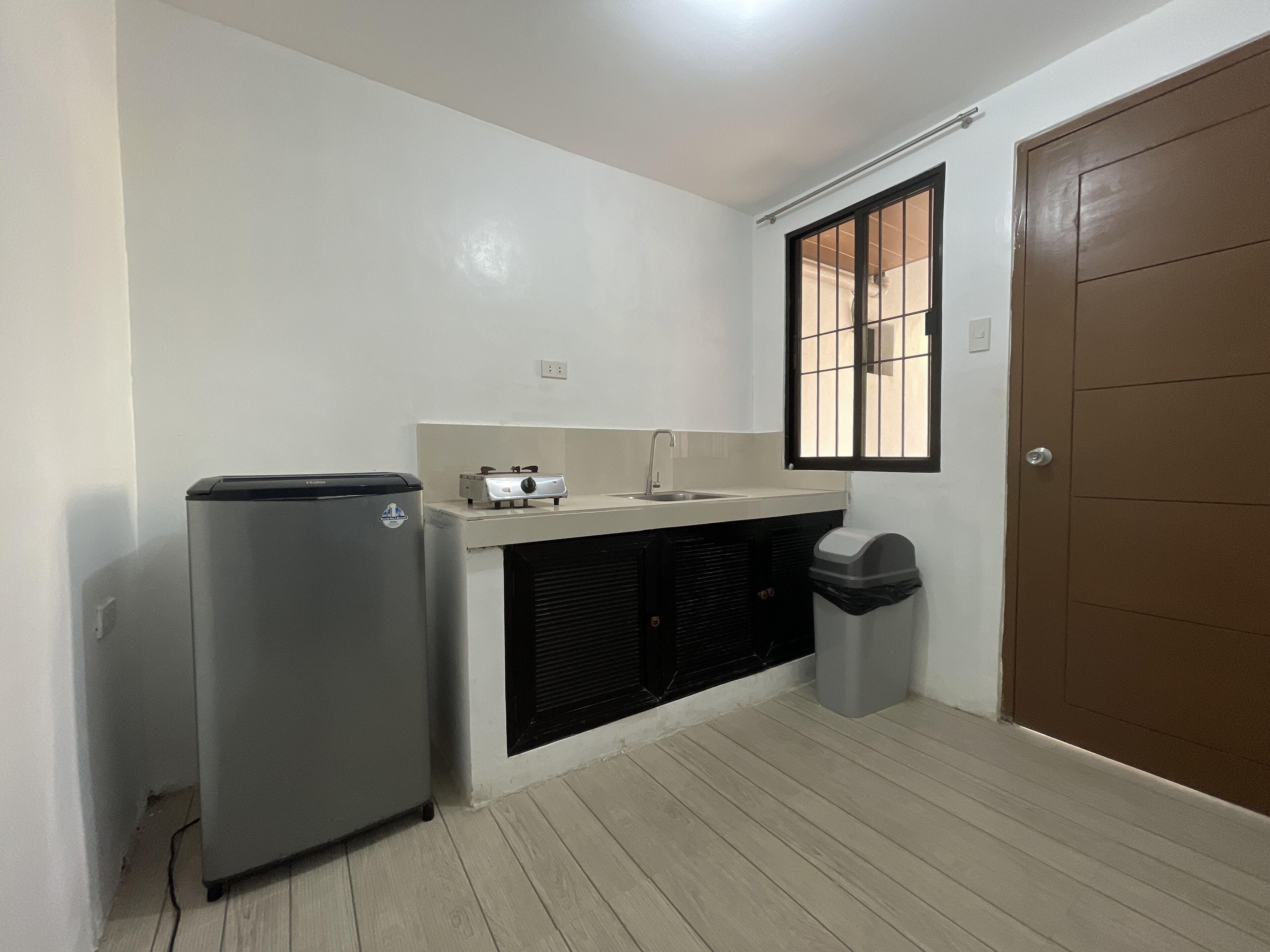 A compact kitchen with a refrigerator, a small countertop, a window with bars, and a door.