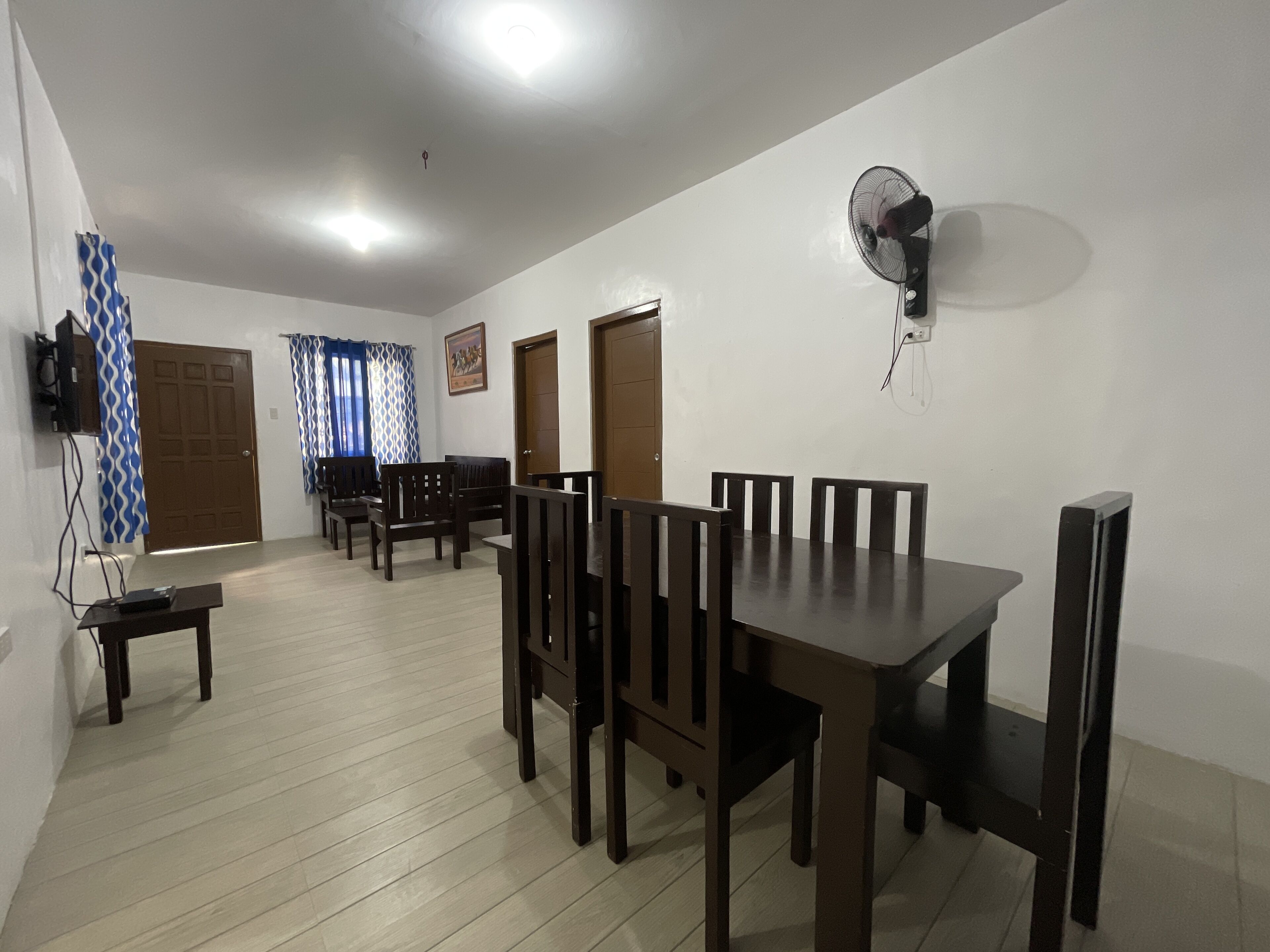 A dining area with a table and chairs, a wall-mounted fan, and a television on the wall.
