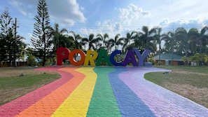 A colorful pathway leading to a sign with the word "PORACAY" in large letters, surrounded by tropical trees and a clear sky. - Poracay Resort (Porac)