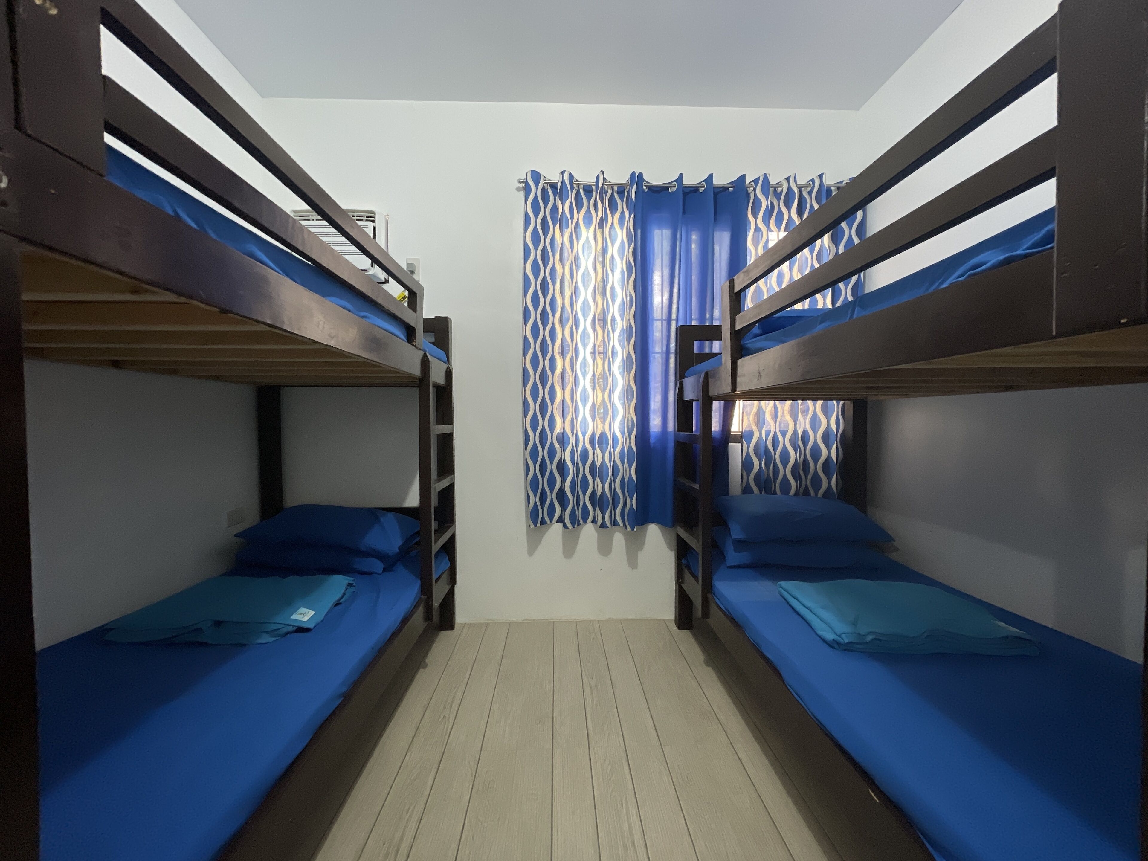 Une chambre avec deux lits superposés, un plancher en bois et un rideau orné d’un motif géométrique.