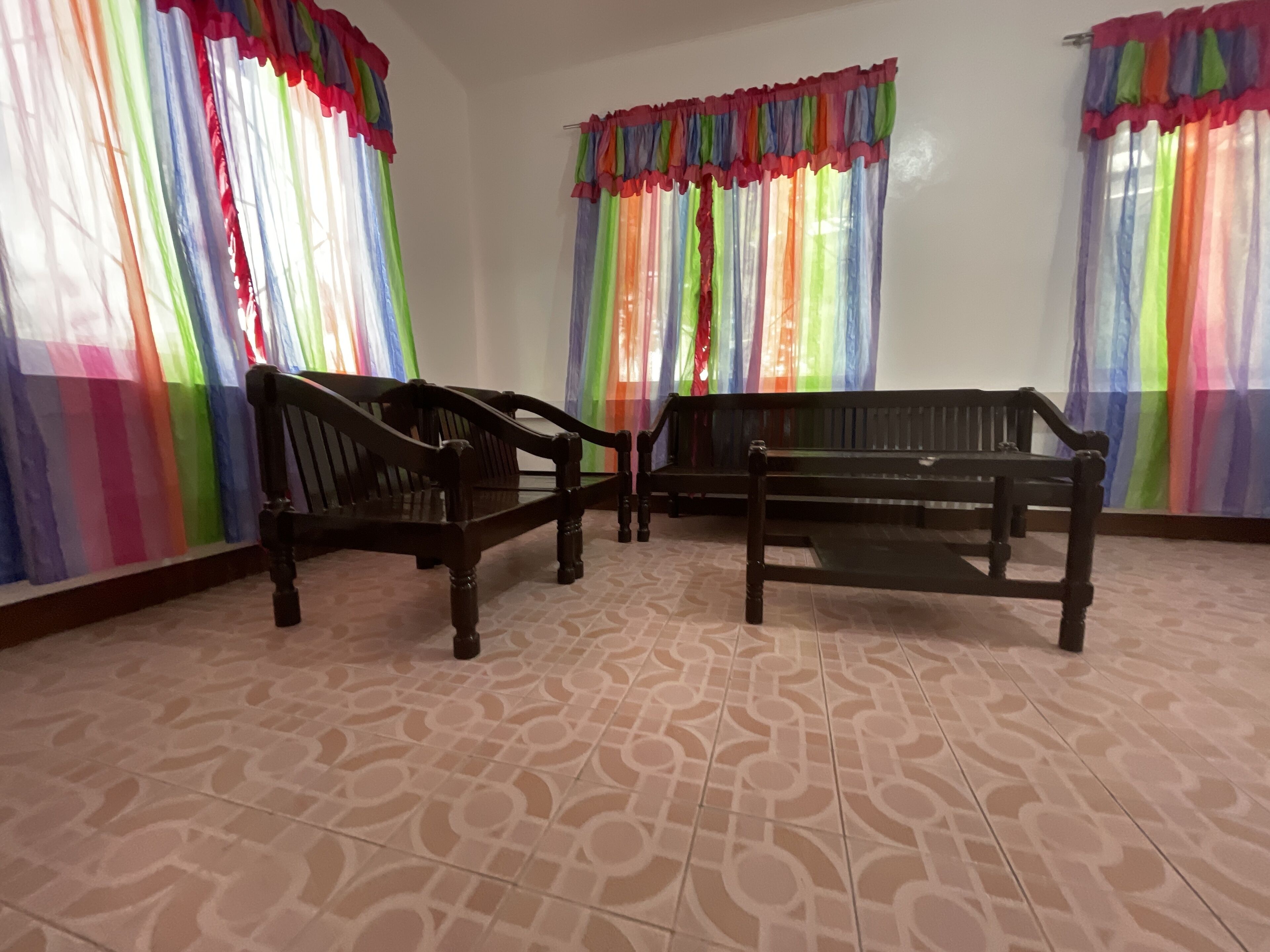 Una habitación con baldosas de suelo estampadas, dos bancos de madera y cortinas coloridas.