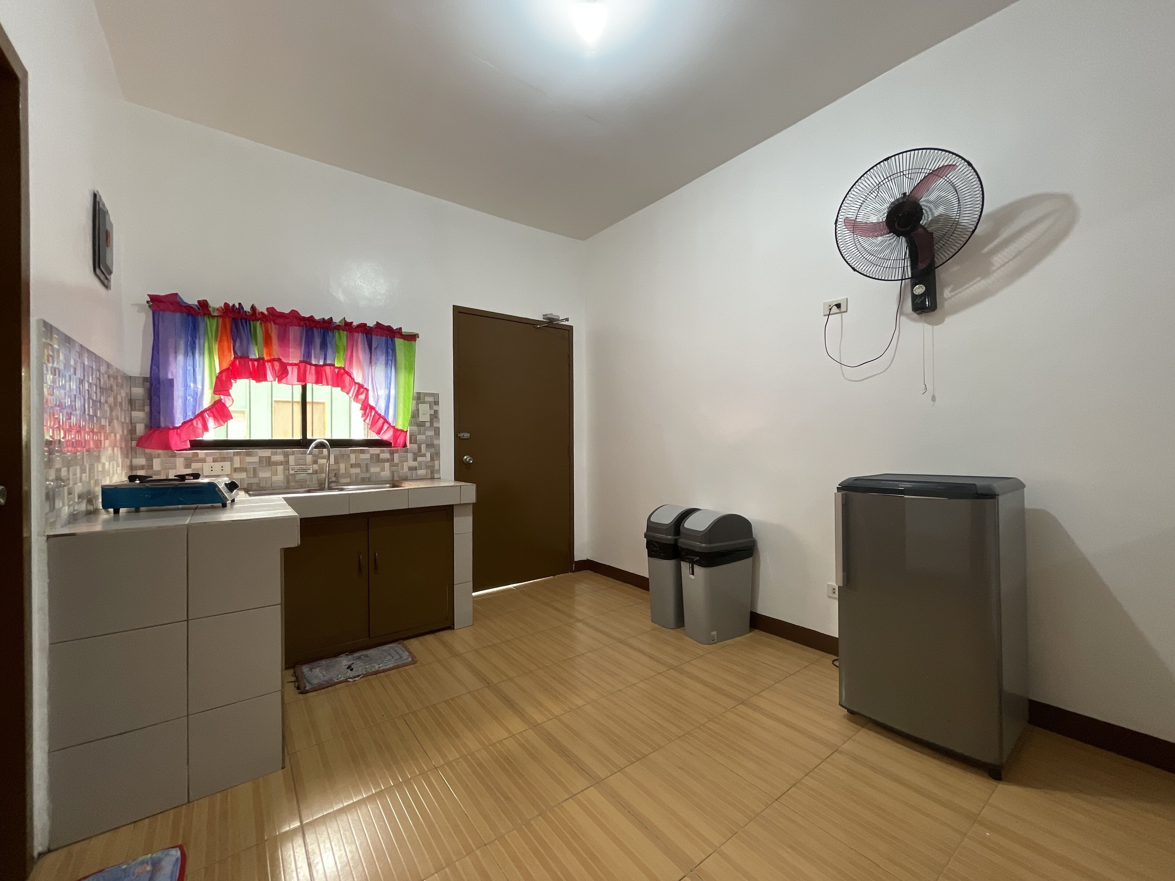 A kitchen with a window, a sink, a stove, a refrigerator, and a trash bin.