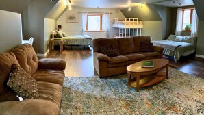 A spacious loft bedroom with a sloped ceiling, a large window, a bunk bed, and a cozy seating area with a couch and coffee table.