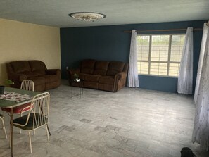 A living room with a brown sofa, a dining table with chairs, a small side table with a plant, and a window with curtains. - Casa campestre donde tocan suavemente los rayos del amanecer! Venga a R-E-L-A-X! (Balcones de la Calera)