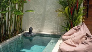 A pool with a floating seat, surrounded by plants, and a pink cushion on a small table. - Oasis Villa 8 by Betterplace (Canggu)