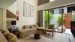 A modern living room with a sofa, armchair, and coffee table. There is a television and a fire extinguisher on the wall. - Oasis Villa 8 by Betterplace (Canggu)