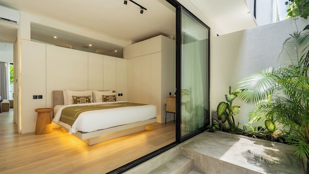 A modern bedroom with a large bed, built-in wardrobe, and a glass door leading to a balcony with plants. - Oasis Villa 8 by Betterplace (Canggu)