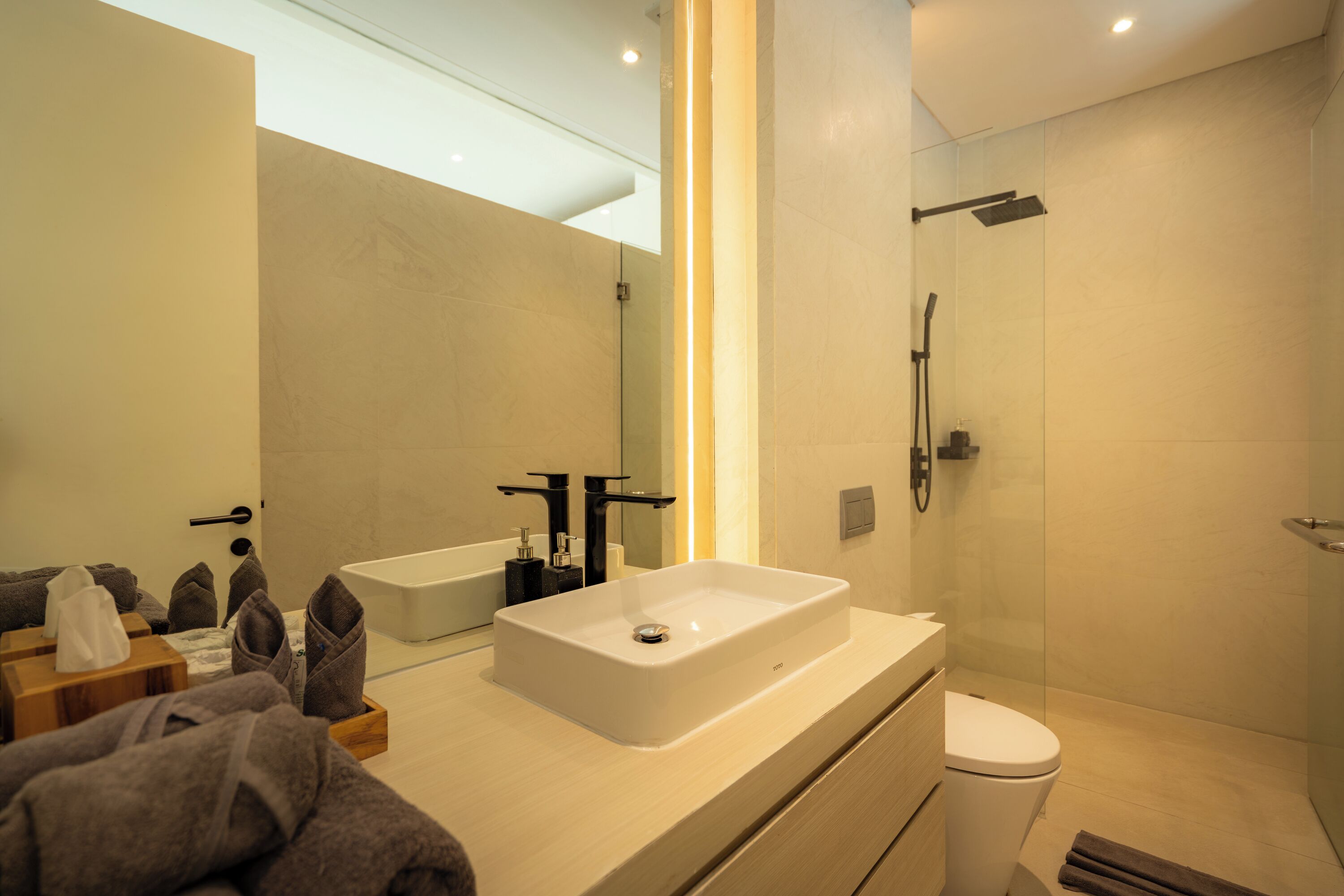 A modern bathroom with a large mirror, a white sink, a toilet, and a shower area.