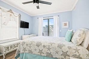 Quarto com cama, ventilador de teto, janela com persianas, televisão e vista para uma varanda.