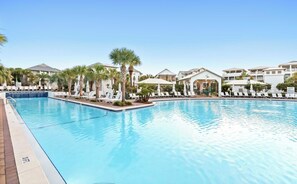 A swimming pool with lounge chairs and palm trees, surrounded by resort-style buildings.
