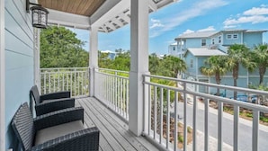 A covered porch with wicker furniture, white railings, and a view of neighboring houses.