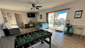 Una sala de estar con una mesa de fútbol de mesa, un sofá, un televisor y una mesa de vidrio con una silla.
